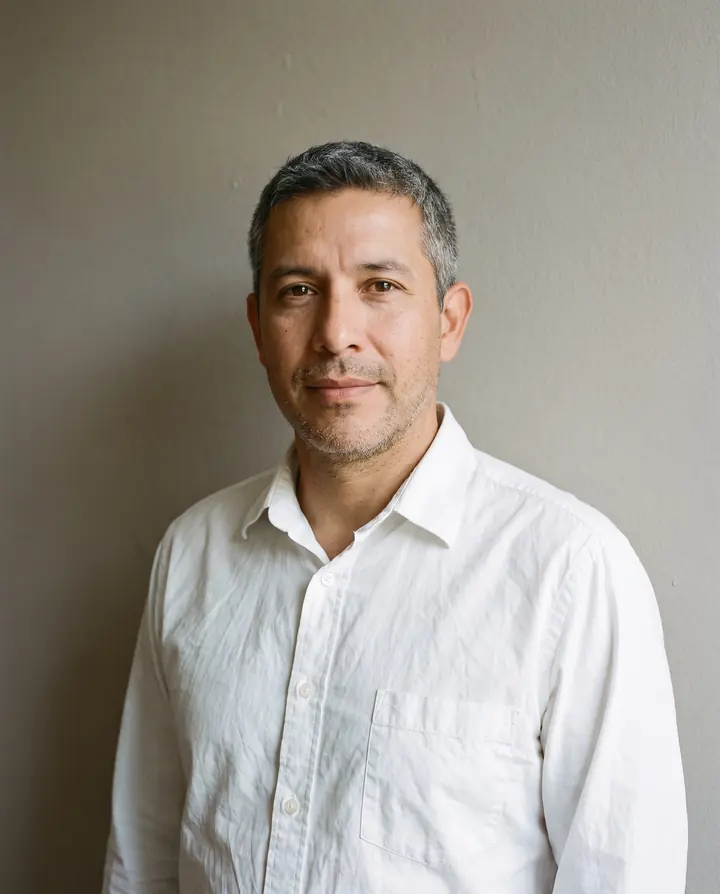 A portrait of a man in a plain white shirt against a plain warm grey wall.